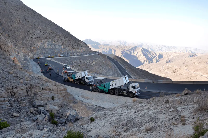 The rental fleet of Al Marwan, notably Volvo and Hino tipper trucks dropping asphalt onto Vogele asphalt-laying pavers on Jebel Jais Road