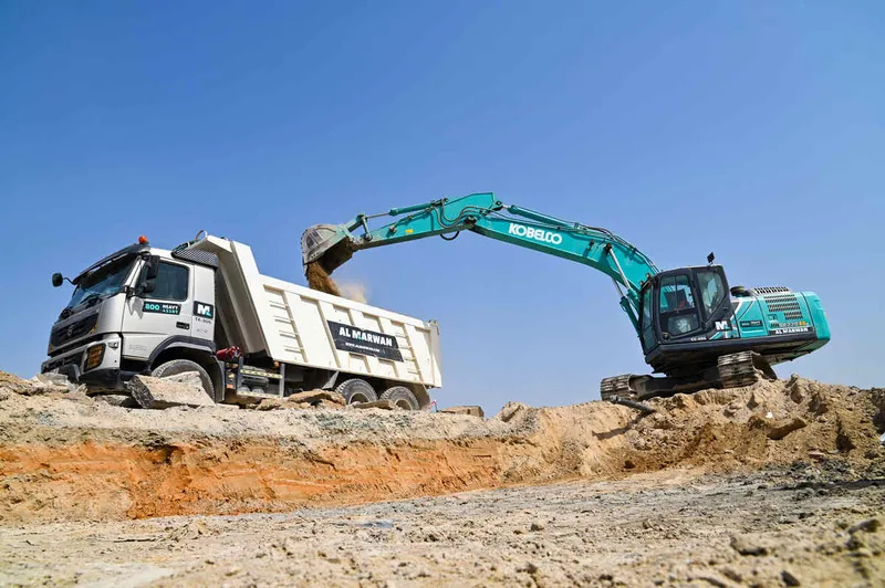 A Kobelco SK220 excavator loading a Volvo 370 rental truck