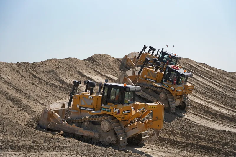 Several CAT and KOMATSU bulldozers at work on a construction site in the desert. Al Marwan Machinery heavy equipment rental fleet.