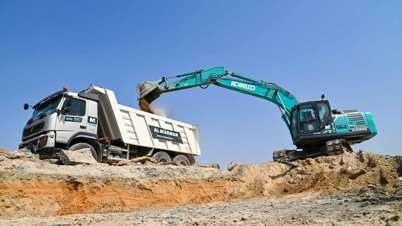 A Kobelco SK220 excavator loading a Volvo 370 rental truck