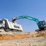 A Kobelco SK220 excavator loading a Volvo 370 rental truck