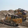 Several CAT and KOMATSU bulldozers at work on a construction site in the desert. Al Marwan Machinery heavy equipment rental fleet.