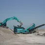 A Kobelco excavator feeding debris into the screener bar hopper