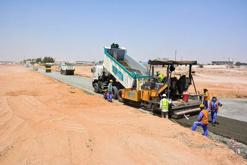 Road building equipment such as the Volvo tipper truck and the Vogele asphalt paver working on Al Jada by Arada property development project